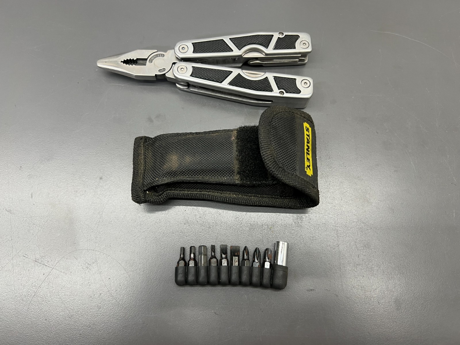 (q) UNUSED STANLEY 2CR 12 IN 1 STAINLESS KNIFE PLIER DRIVER W CASE & BITS