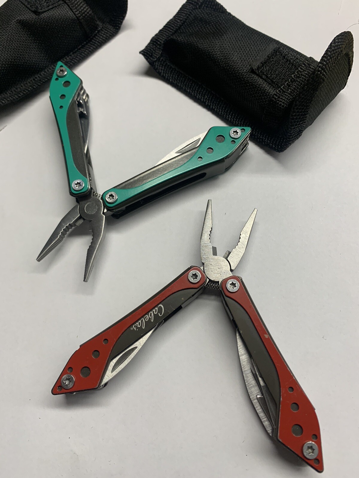 Two Cabela’s Multi Tools, Teal And Red, With Black Cases